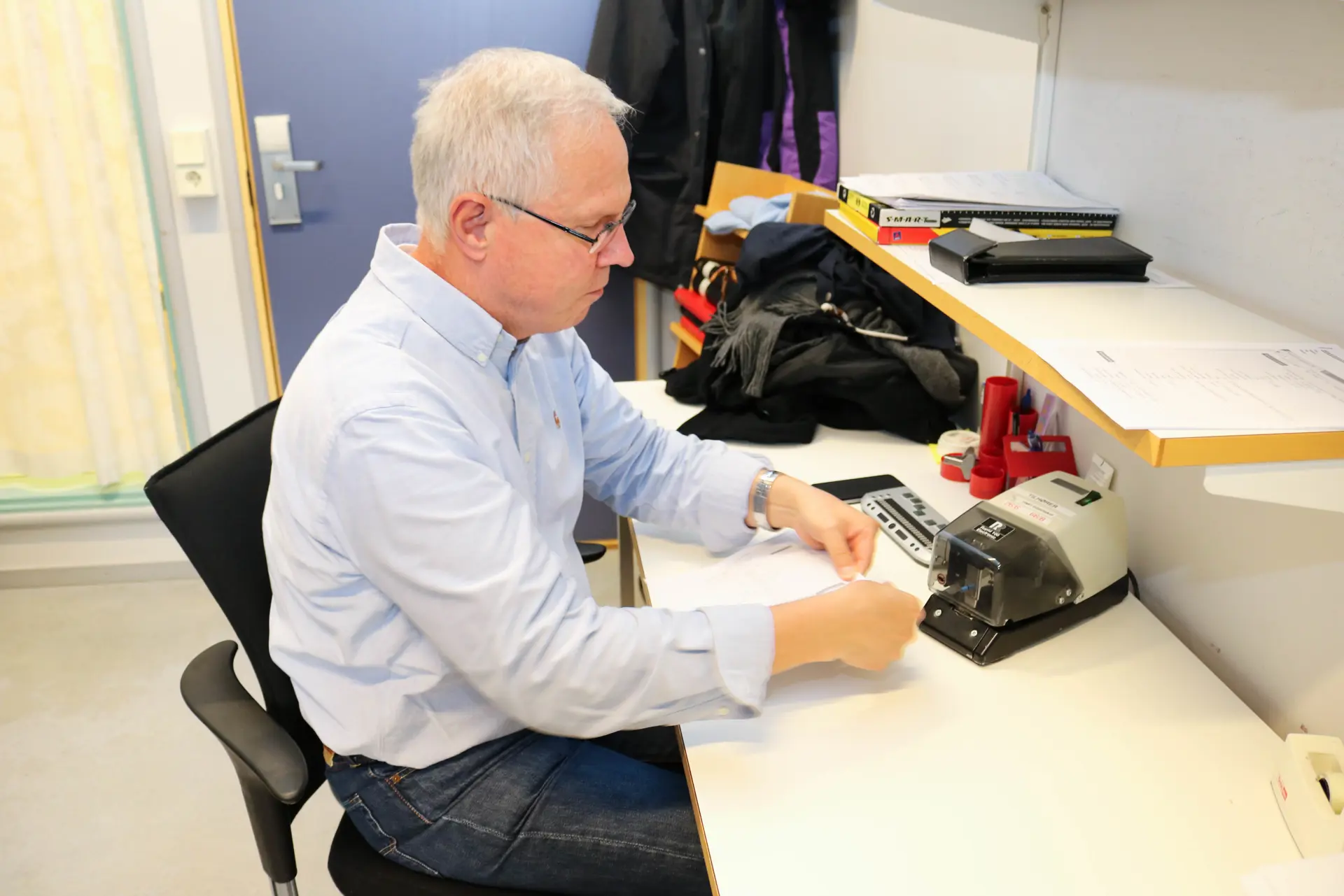 En mann som sitter ved et skrivebord og stifter sammen ark